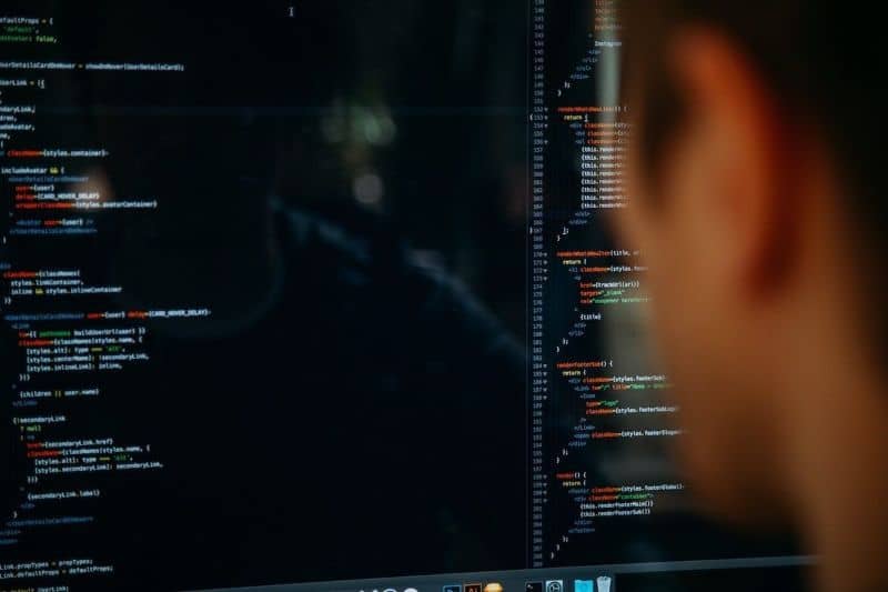 Hombre frente a una pantalla negra con mucho código